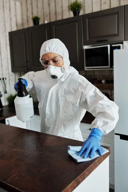 who-we-are Une personne portant des gants en caoutchouc nettoie une cuisinière sale avec un chiffon et un vaporisateur.